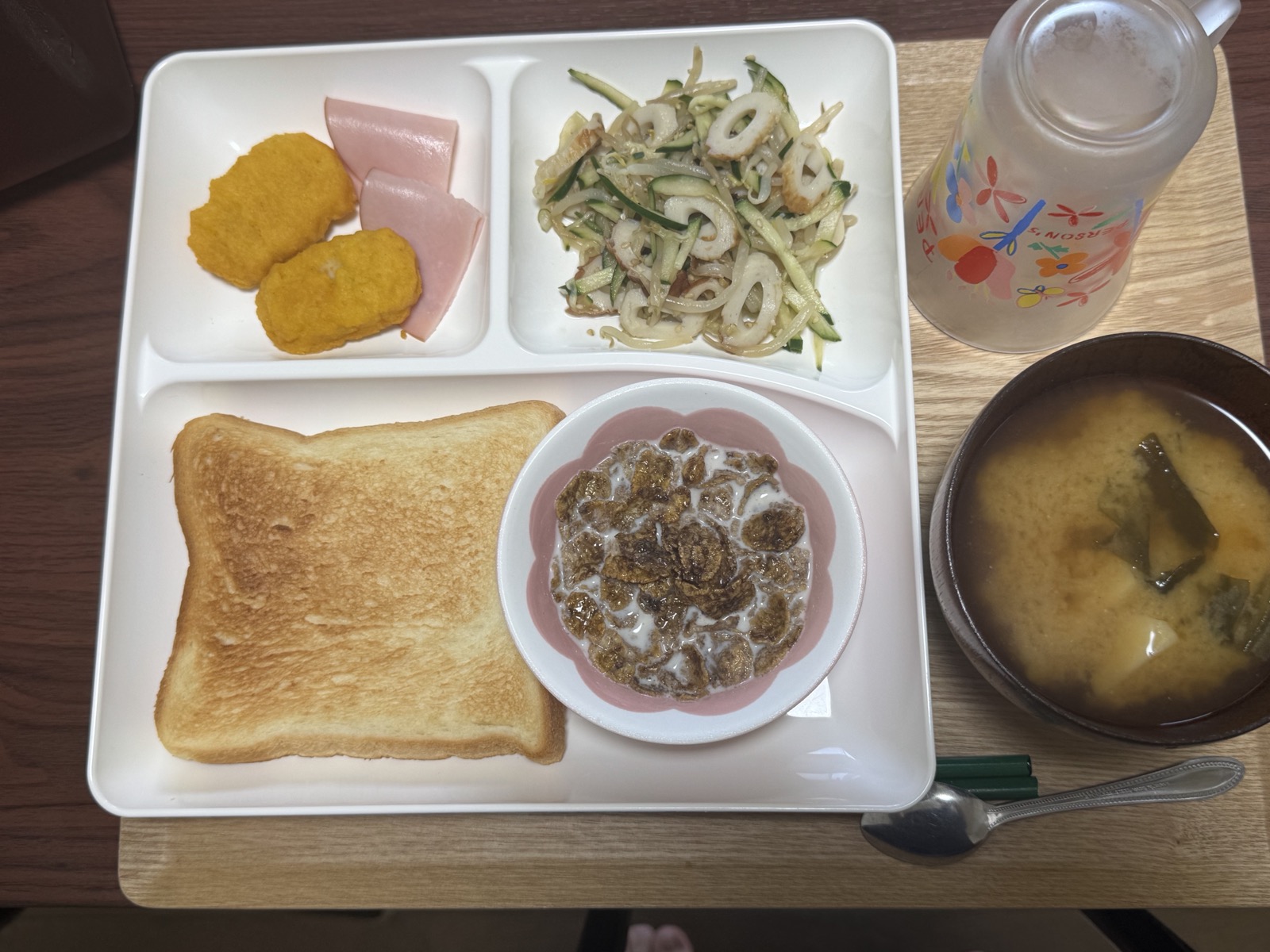 にこにこビレッジで提供している朝食の一例。トースト、コーンフレーク、ナゲットとハム、ちくわときゅうりの和え物、味噌汁