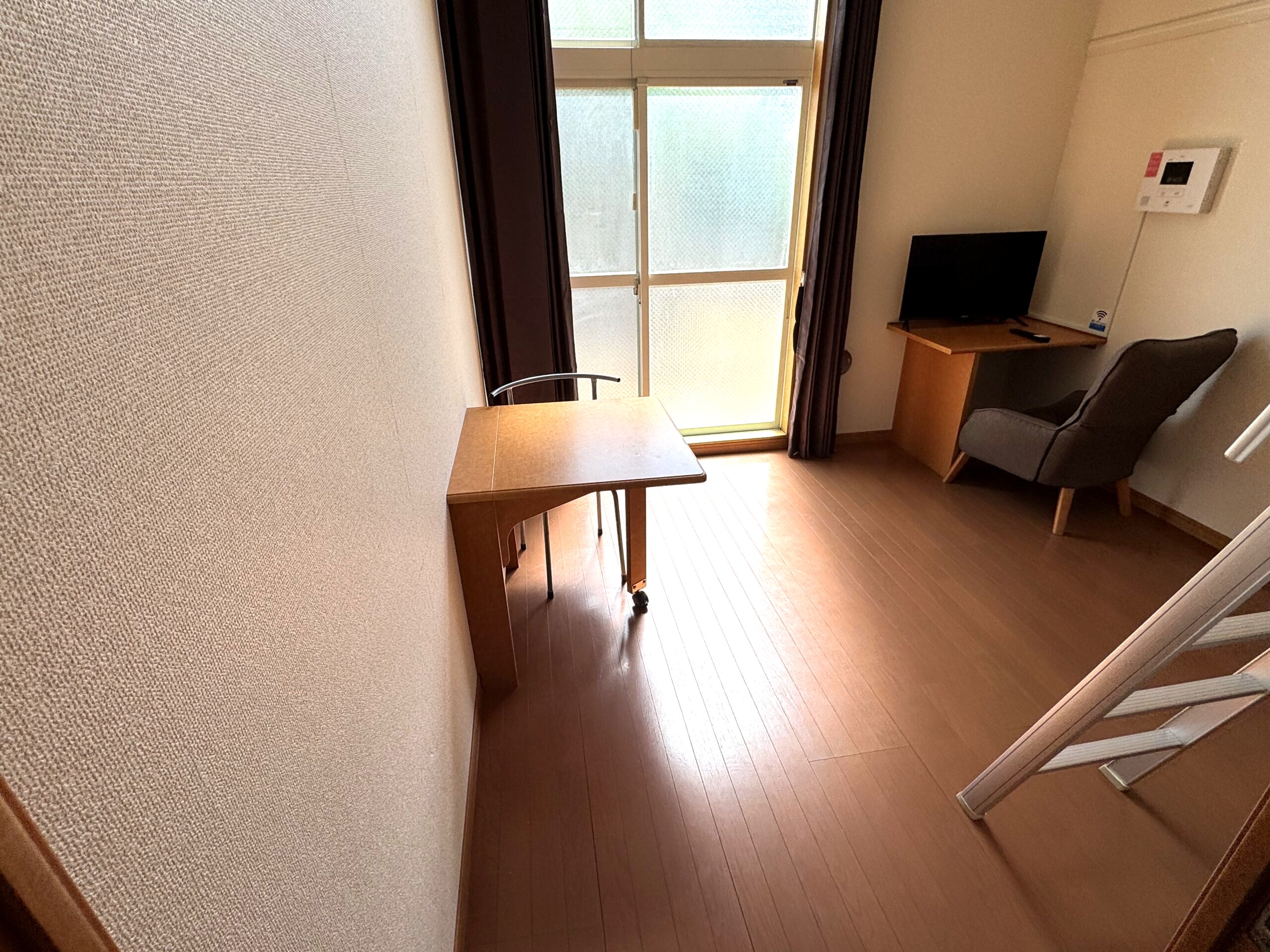 にこにこビレッジ永国サテライトの居室。掃き出し窓、テーブル、デスクとテレビ、一人掛けソファ